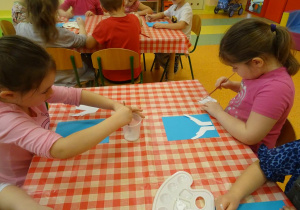 Dzieci naklejają elementy z białego papieru.